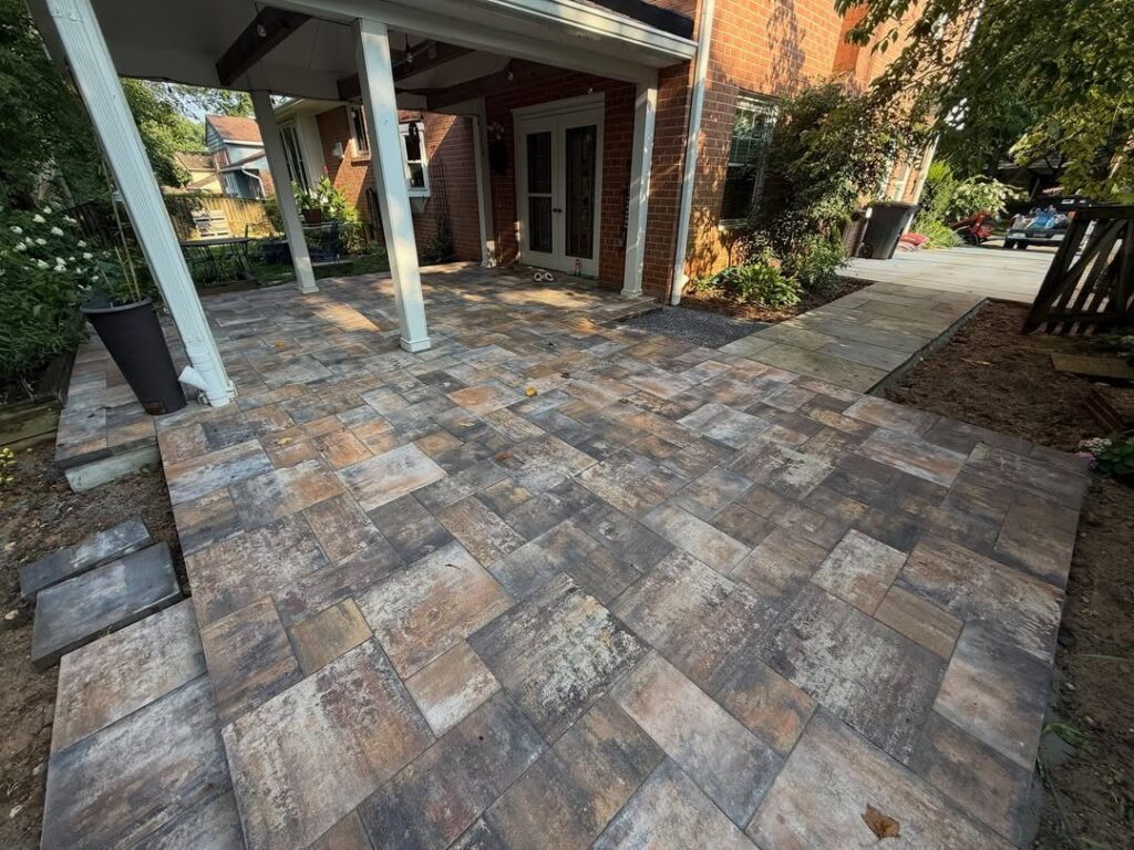 Stone pavers in various earth tones forming a new patio under a white porch structure.