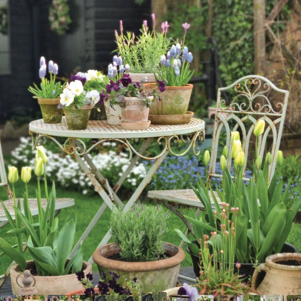 Potted spring flowers and greenery arranged on a white wrought iron garden table outdoors.