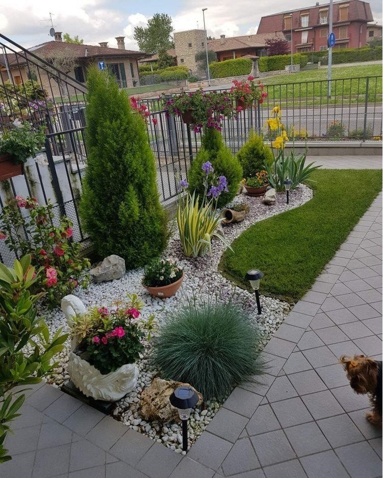 A small landscaped front yard with white gravel, green shrubs, grass, and decorative garden lights.